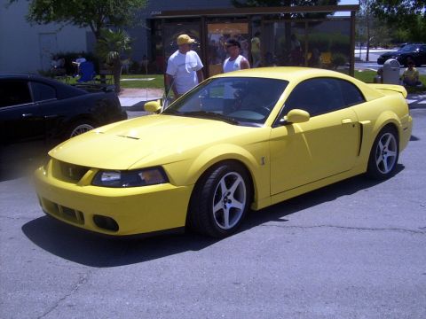 2002 Ford Mustang - A yellow 2002 Ford Mustang is parked on asphalt with a black car beside it.