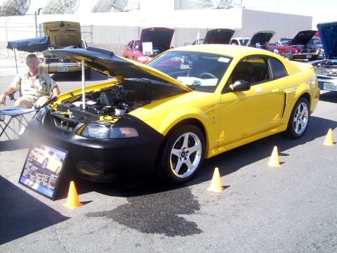 2002 Ford Mustang - A yellow coupe with its hood open is displayed at an outdoor event with other vehicles in the background.