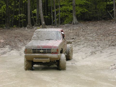 1979 Ford Bronco - This red pickup truck navigates a challenging muddy course, its tires deep in the mire.