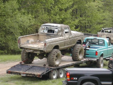 1979 Ford Bronco - A heavily mud-covered pickup truck is being transported on a trailer, with other vehicles visible in the background.