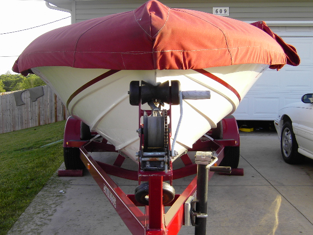 White boat with red cover on maroon trailer, bow winch visible, parked on driveway