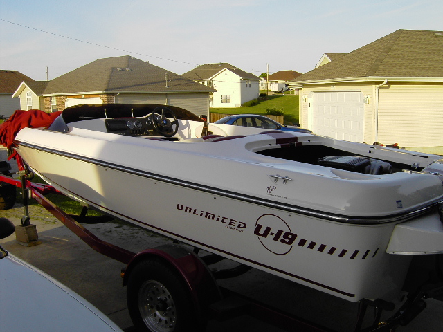 White Four Winns speedboat on maroon trailer in driveway, rear quarter view