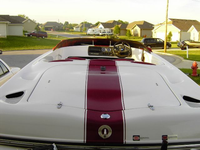 Rear of white boat with maroon stripe parked in a suburban driveway