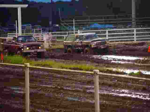 Two trucks racing through mud at an event