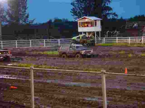 1978 Ford Bronco - Vehicles navigate a muddy track during an event, with spectators in a booth overlooking the scene.