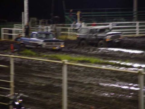 1978 Ford Bronco - Two vehicles compete in a mud race, with a blue pickup truck in the foreground and a dark SUV behind it.
