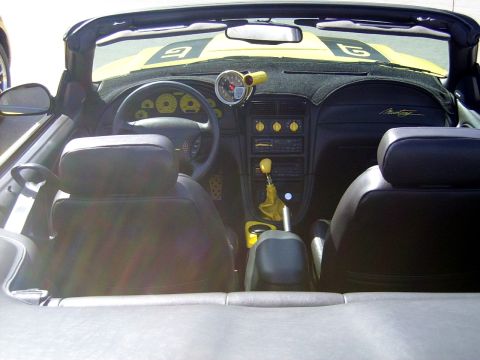 2002 Ford Mustang - The interior of a yellow convertible shows a custom gauge pod and yellow accents on the shifter and dashboard knobs.