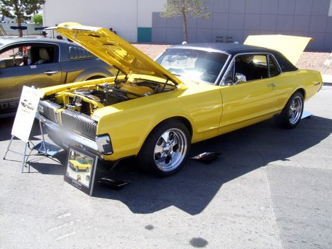 2002 Ford Mustang - A yellow 1969 Mercury Cougar XR7 is displayed with its hood and trunk open, parked next to a modern Ford Mustang.