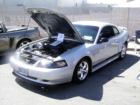 2002 Ford Mustang - A silver 2002 Ford Mustang is displayed with its hood open, revealing the engine and a sign. Another Mustang is visible in the background.