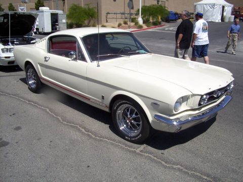 2002 Ford Mustang - A white 1965 Ford Mustang coupe is parked next to another vehicle with its hood up.