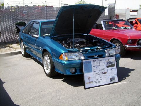 2002 Ford Mustang - Teal 1993 Ford Mustang SVT Cobra coupe displayed with its hood open, alongside a red convertible and an orange car.