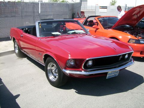 2002 Ford Mustang - A classic red convertible is parked next to a modern orange car with its hood open.