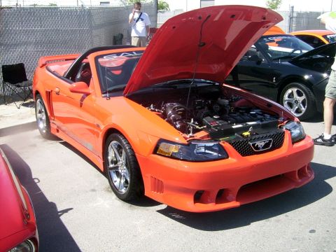 2002 Ford Mustang - An orange convertible sports car is parked with its hood open, revealing the engine bay.