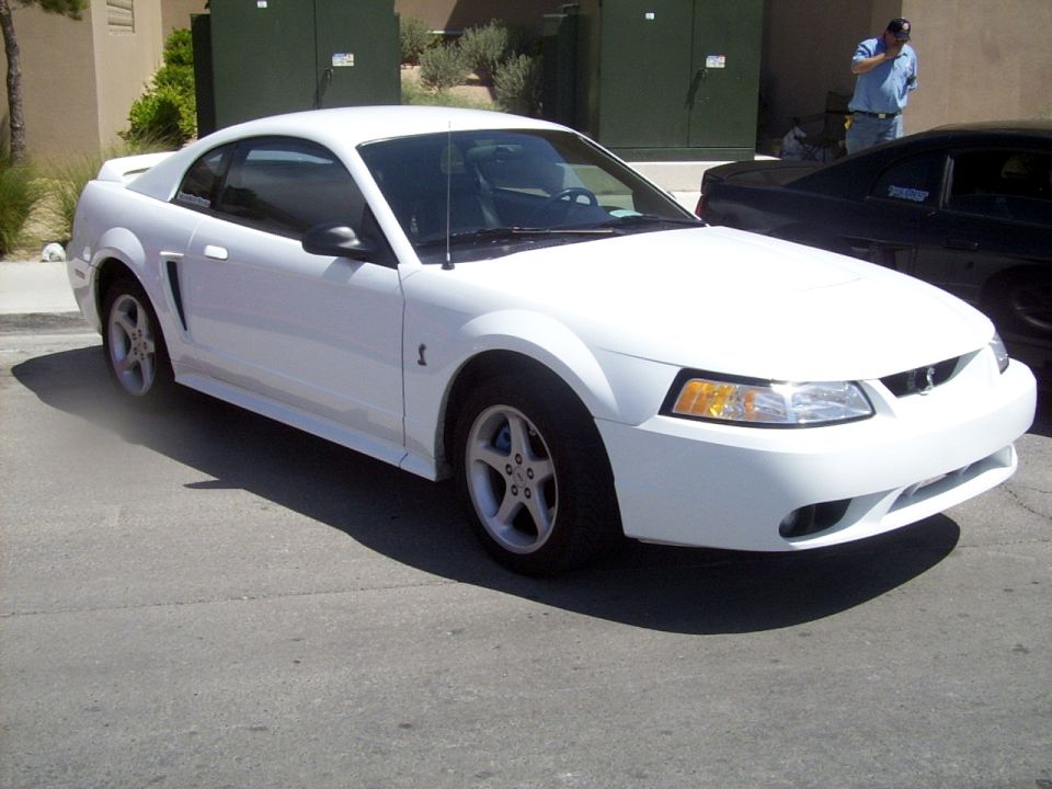 White 2002 Ford Mustang parked on asphalt, black car behind it
