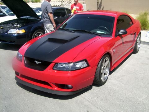 2002 Ford Mustang - A red Ford Mustang is parked at an outdoor event, with another vehicle's hood open in the background.