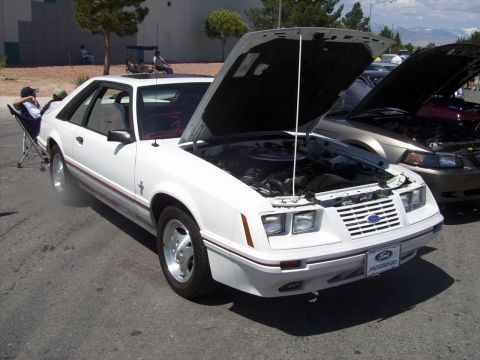 2002 Ford Mustang - A white 1987 Ford Mustang hatchback is displayed with its hood open, parked next to another vehicle.