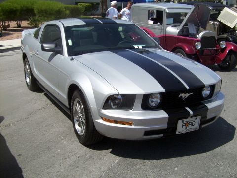 2002 Ford Mustang - This silver Ford Mustang with black racing stripes is parked outdoors next to other vehicles.
