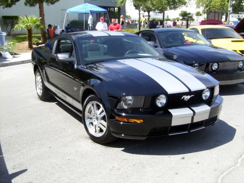 2002 Ford Mustang - A black 2005 Ford Mustang GT with silver racing stripes is parked outside, with another Mustang and a yellow car visible in the background.