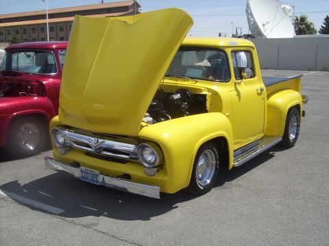 2002 Ford Mustang - A bright yellow 1956 Ford F-100 pickup truck is displayed with its hood open, parked next to another vintage truck.