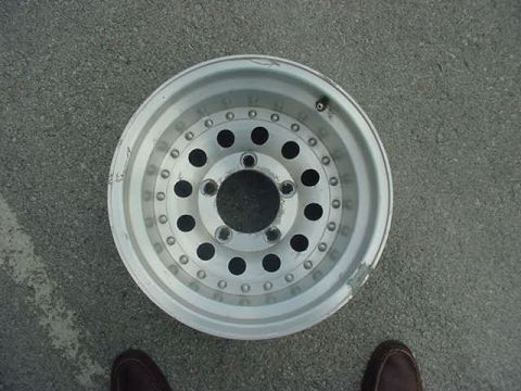 1995 Ford Bronco - Close-up of an aftermarket aluminum wheel lying on asphalt.