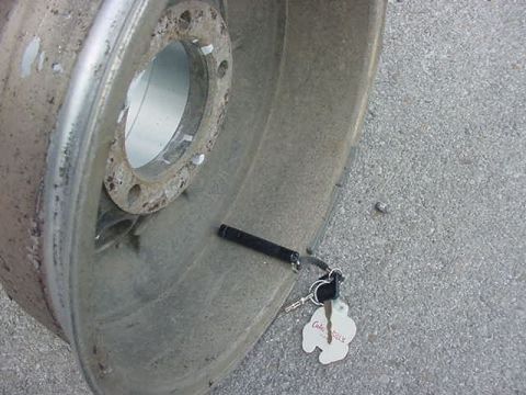 1995 Ford Bronco - A close-up of a damaged aluminum wheel rim with keys and a tag on the ground.