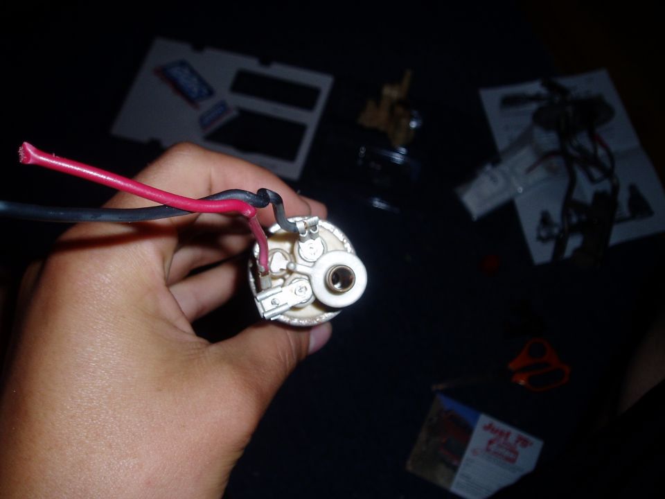 Fuel pump with red and black wires held in hand. Papers and scissors in background