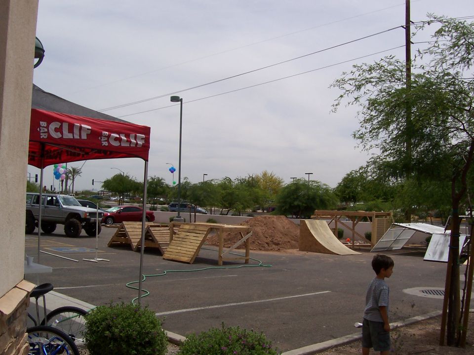 Silver SUV parked near a red Clif Bar tent with wooden ramps and a dirt pile in a parking lot