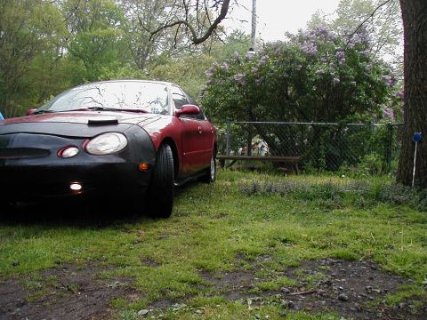 1997 Ford Taurus - A red sedan is parked in a yard with a car bra on its front end.