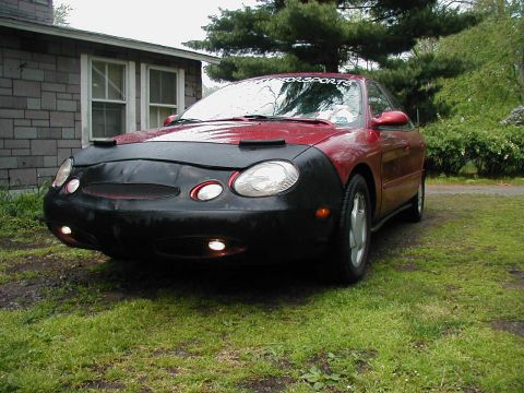 1997 Ford Taurus - A red sedan is parked in front of a house, partially covered by a car bra.