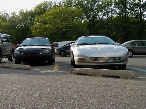 1997 Ford Taurus - Two cars are parked in a lot, with trees in the background.