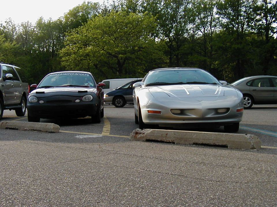 Silver sports car parked in front of a black sedan in a parking lot