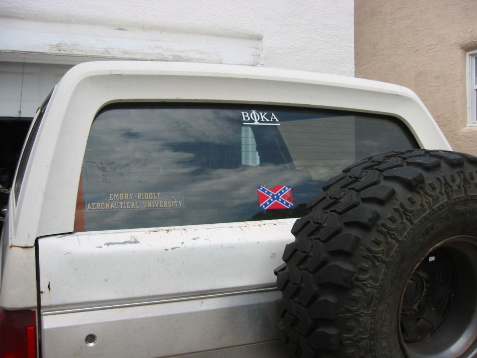 Rear window of white Bronco with Embry-Riddle and Confederate-flag decals and spare tire