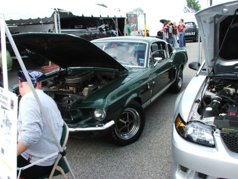 2005 Ford Mustang - A classic green Mustang fastback is displayed with its hood open, alongside a newer model silver car.