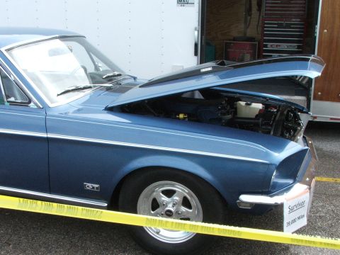 2005 Ford Mustang - Classic blue car with hood open, GT badge on fender, yellow tape in front.