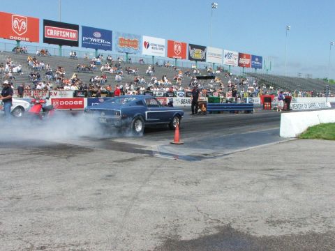 2005 Ford Mustang - A blue muscle car performs a burnout on the drag strip, creating a cloud of smoke.