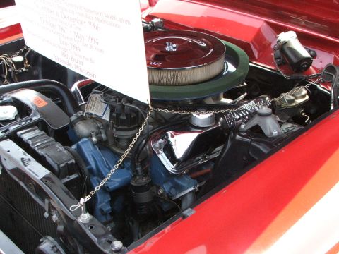 2005 Ford Mustang - The engine bay of a red 1966 Ford Mustang, a prominent air cleaner and an informational card detailing its history.