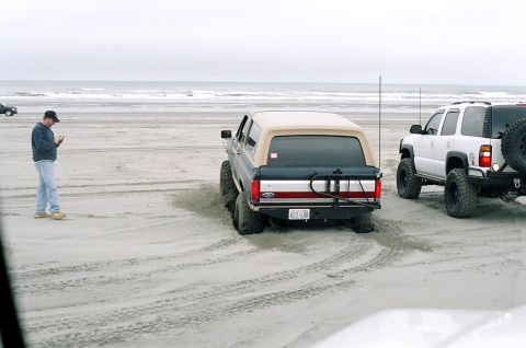 1979 Ford Bronco - A Ford Bronco and a white SUV are parked on a sandy beach near the ocean.