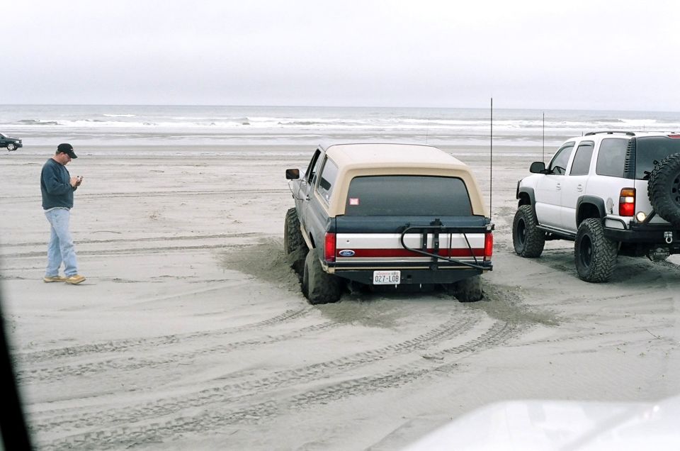 Gray Ford Bronco with tan top stuck in sand, rear view. Red stripe on tailgate