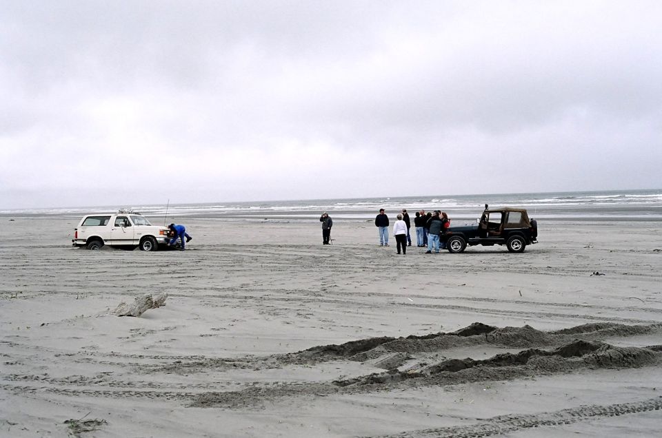 White 1987 Ford Bronco stuck in sand with a person checking the engine