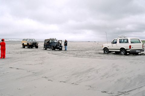 1979 Ford Bronco - Three SUVs are parked on a sandy beach under an overcast sky.