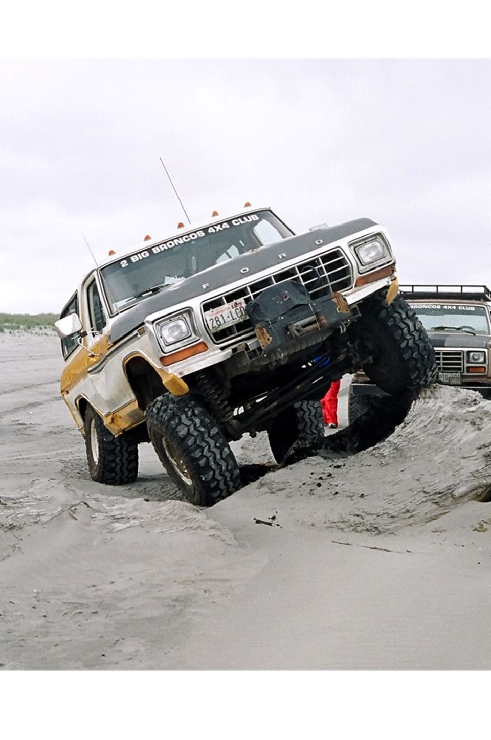 Ford Bronco climbing a sand dune, another Bronco behind it. Text on windshield says '2 BIG BRONCOS 4X4 CLUB'