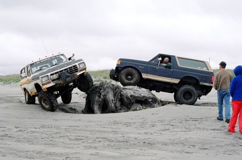 1979 Ford Bronco - Two 1979 Ford Broncos tackle challenging terrain on a sandy beach, demonstrating their off-road capabilities.
