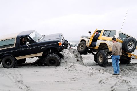 1979 Ford Bronco - Two Ford Broncos navigate a sandy terrain, one appears to be stuck.