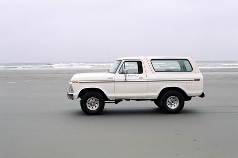1979 Ford Bronco - Side view of a white Ford Bronco on a beach, with "Ford" text on the door.