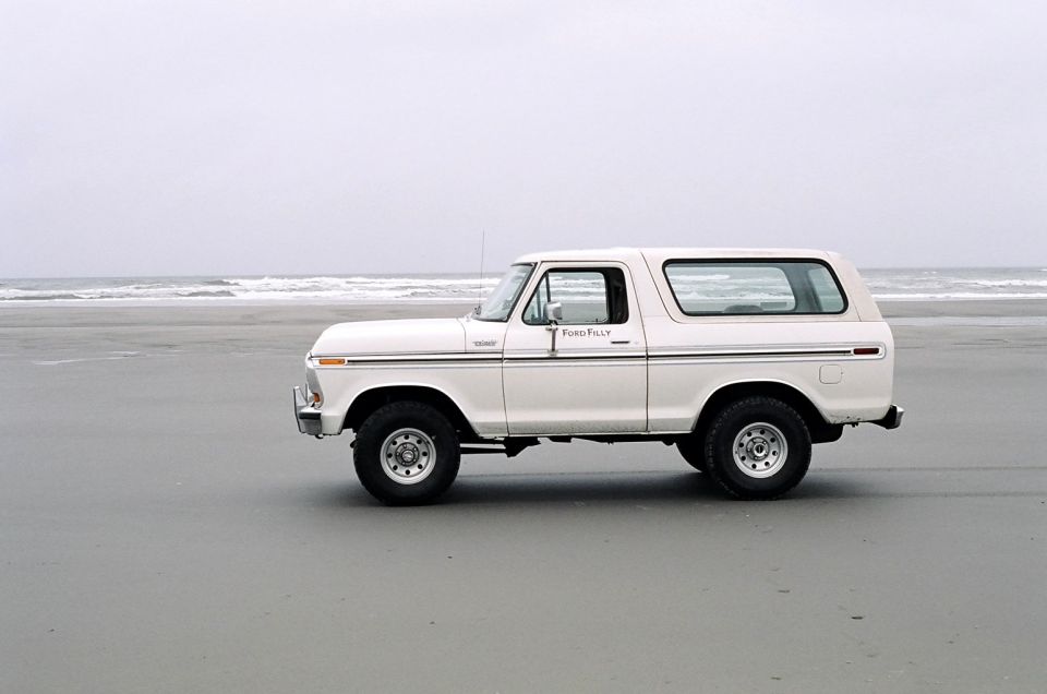 White Ford Bronco with Ford Filly door lettering parked on a beach by the surf