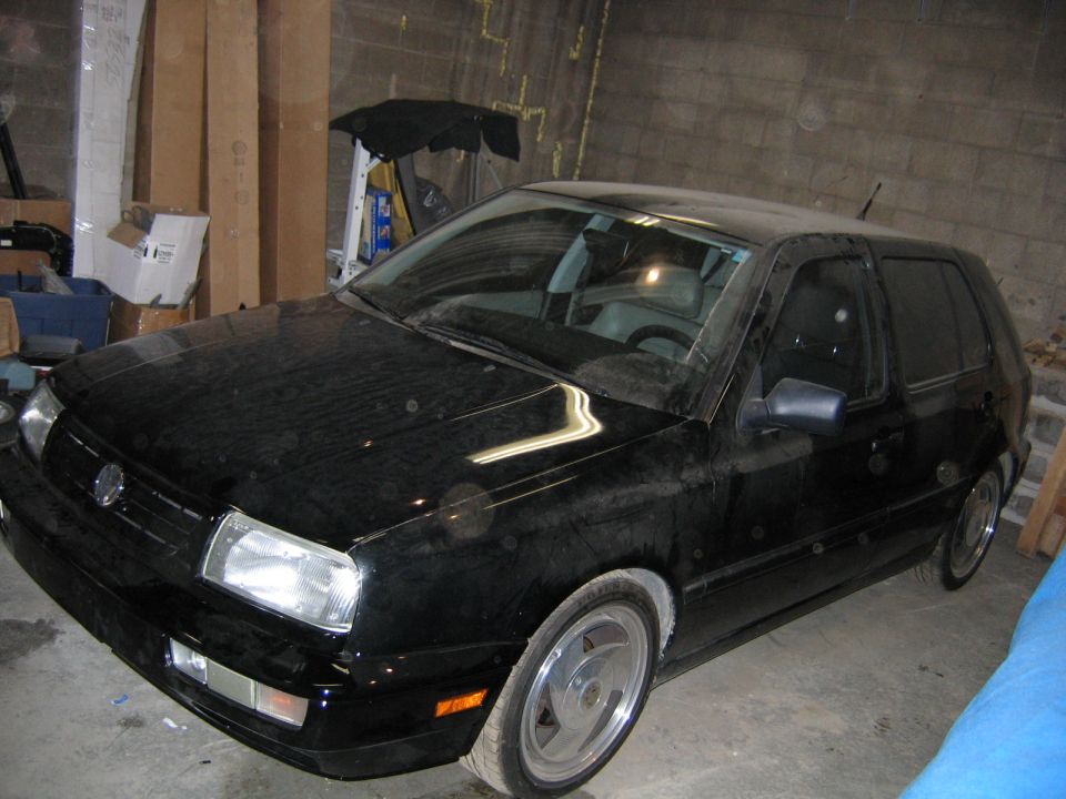 Black Volkswagen Golf Mk3 parked indoors. Front grille and headlights are visible