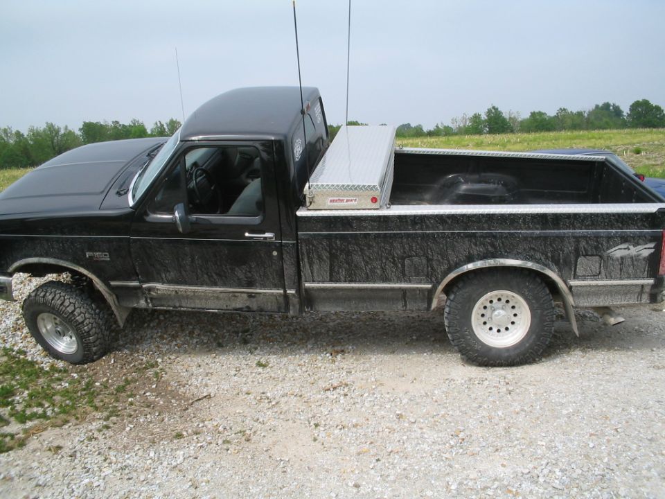 Black pickup truck with a toolbox in the bed, parked on a gravel surface