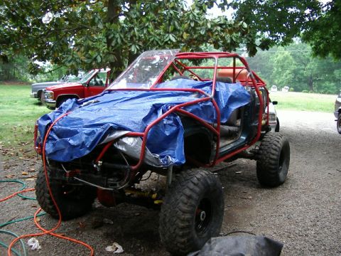 1985 Ford Bronco - This custom off-road vehicle is partially covered with a blue tarp and has a prominent red roll cage.