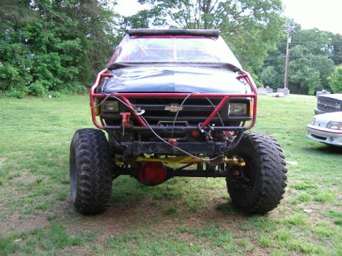 1985 Ford Bronco - This heavily modified off-road vehicle features oversized tires and a prominent red roll cage, obscuring its original make and model.
