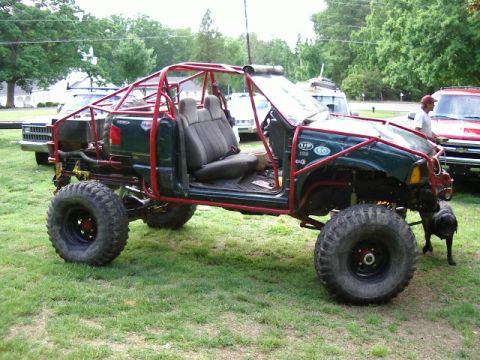 1985 Ford Bronco - Modified off-road vehicle with extensive roll cage and large tires, parked on grass.